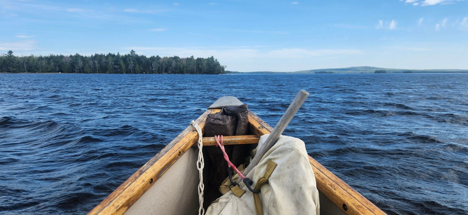 Canoe heading toward shoreline on East Grand Lake under a blue sky in Maine.
