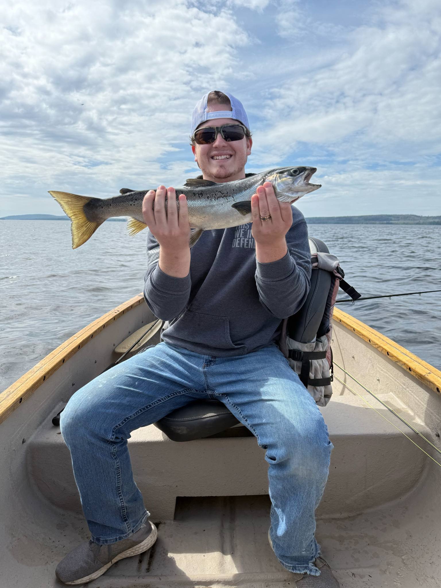 Smiling fisherman holding a freshly caught salmon aboard a grand laker canoe on East Grand Lake