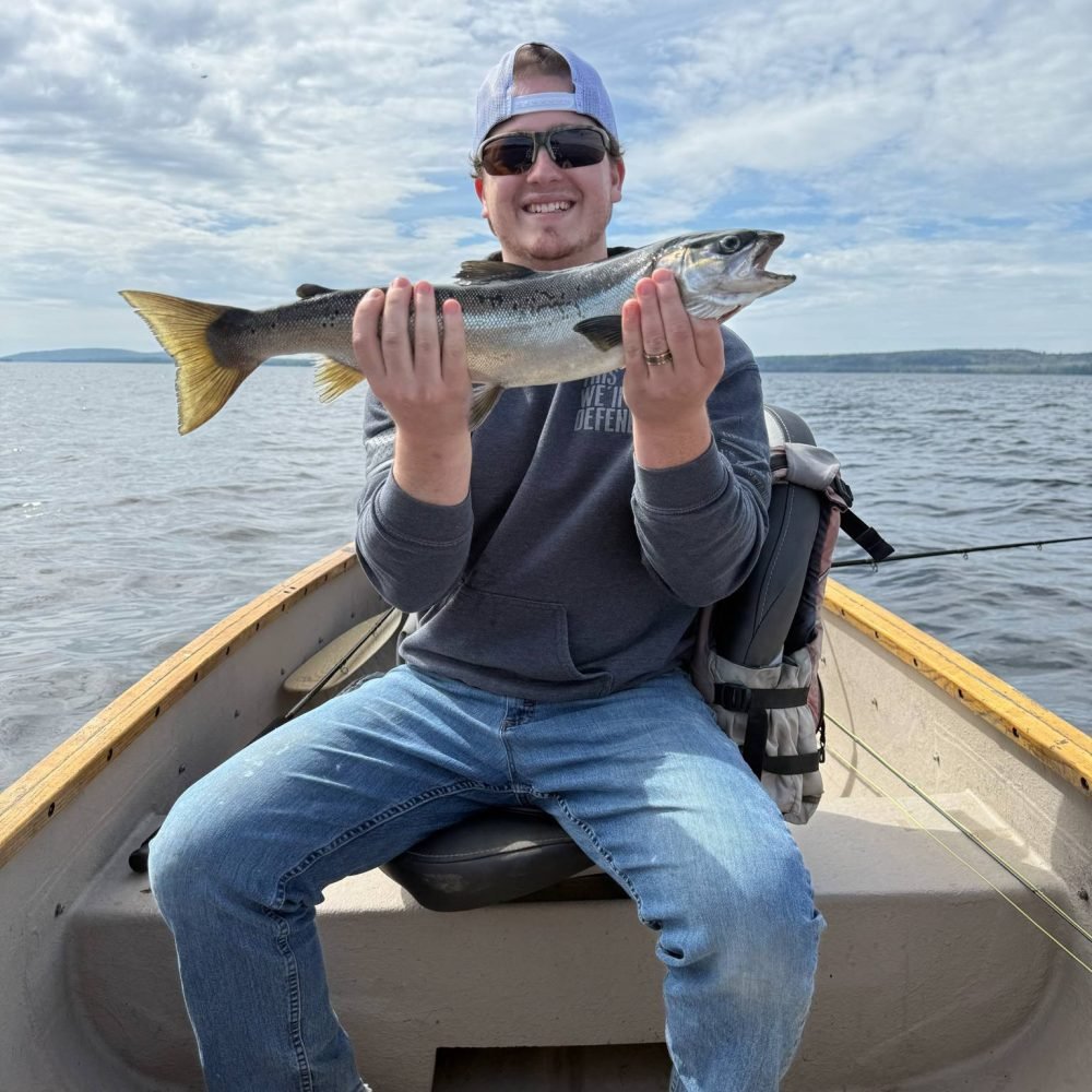 Smiling fisherman holding a freshly caught salmon aboard a grand laker canoe on East Grand Lake